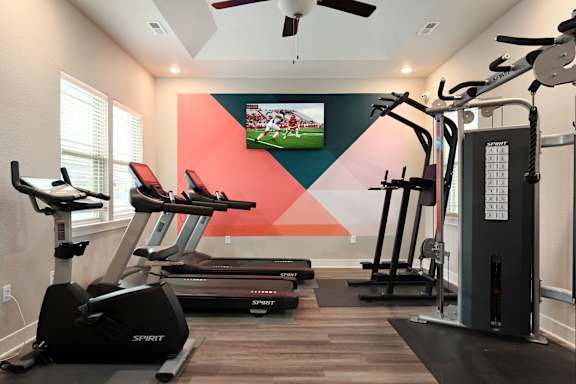 A gym with treadmills, elliptical machines, and a television playing a football game.