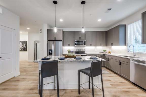 A modern kitchen with a center island, two chairs, and pendant lights.
