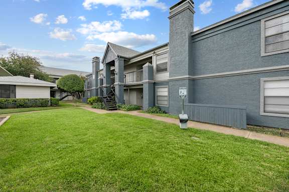 A grassy area in front of a grey building with a sign on a post.