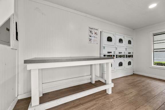 A white bench with a grey top is in the middle of a room with a white wall and a window.