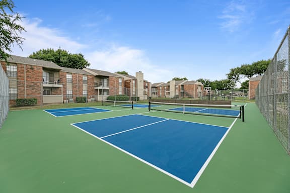 A tennis court is surrounded by apartment buildings.