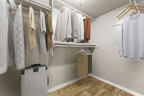 A white closet with clothes hanging and a suitcase.
