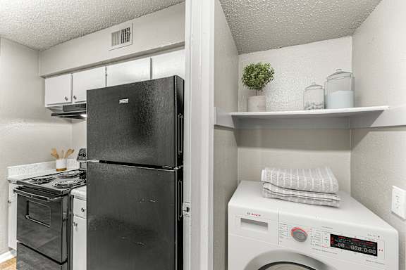 A black refrigerator is in a kitchen with a washer and dryer.