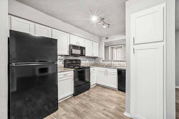 A black refrigerator stands in a kitchen with white cabinets and a black stove.