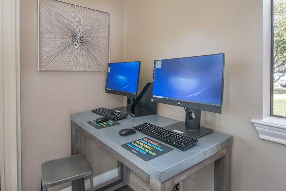a computer desk with two monitors and a keyboard and mouse on it at Polo Clubs Apartments, Austin, TX