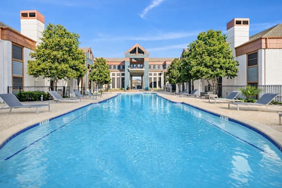 A large swimming pool in front of a building with trees on the side.
