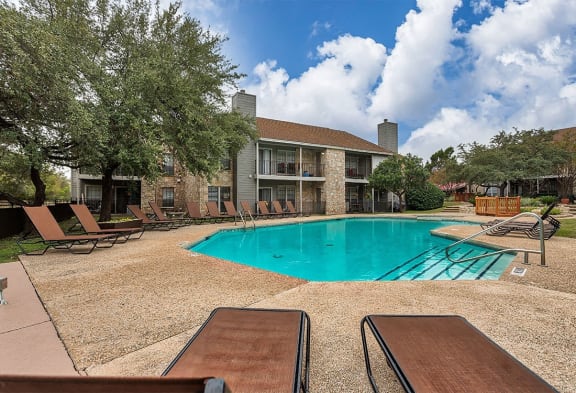 a swimming pool with chairs around it in front of a house at The Broadwater at Salado Creek, San Antonio, TX, 78216