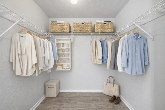A white closet with clothes hanging and baskets on the shelf.