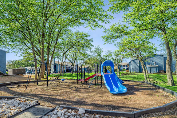 A playground with a blue slide and trees.