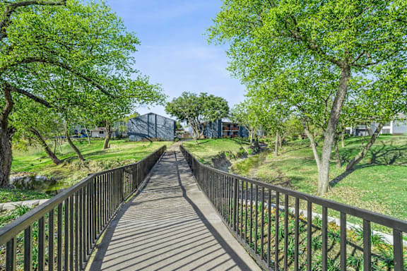 A wooden walkway with metal railings leads through a lush green park.