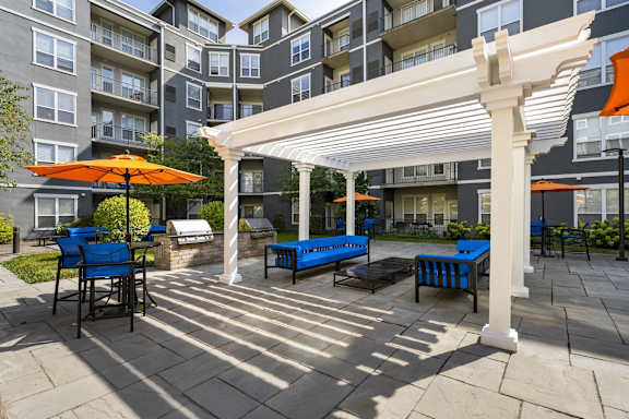 A patio with a white pergola and blue chairs.