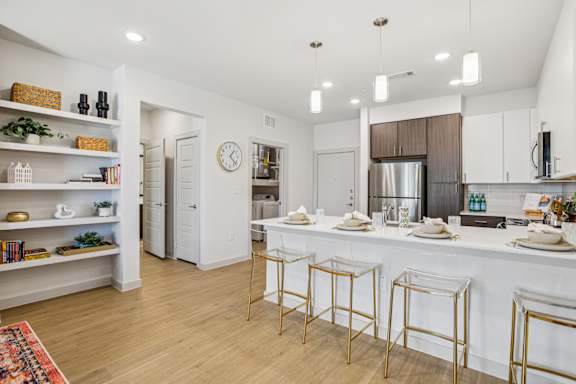 A kitchen with white cabinets and a white island with gold bar stools at ThreeTwenty at the Vybe Apartments, Kyle, Texas