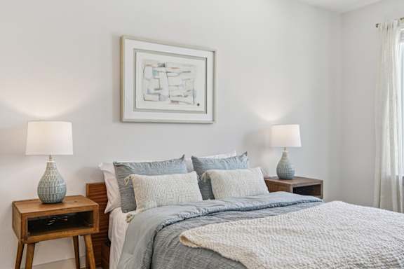 A bedroom with a bed, two lamps, and a painting on the wall at ThreeTwenty at the Vybe Apartments, Kyle, TX