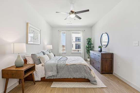A bedroom with a bed, nightstand, and a ceiling fan. at ThreeTwenty at the Vybe Apartments, Texas