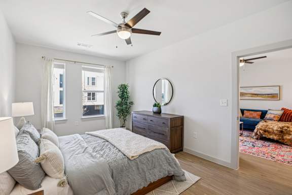 A bedroom with a bed, dresser, mirror, and a ceiling fan. at ThreeTwenty at the Vybe Apartments, Kyle