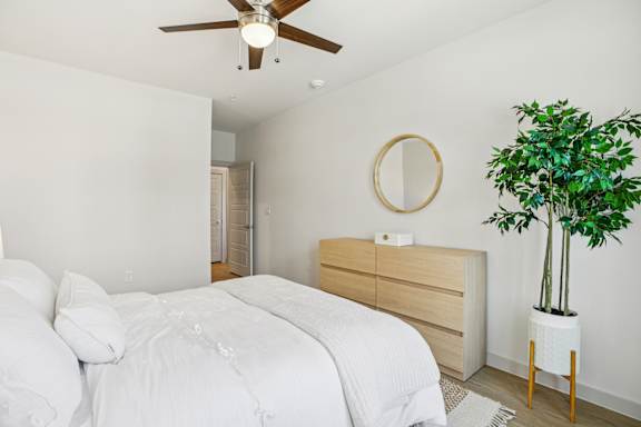 A bedroom with a bed, dresser, mirror, and plant. at ThreeTwenty at the Vybe Apartments, Kyle, 78640
