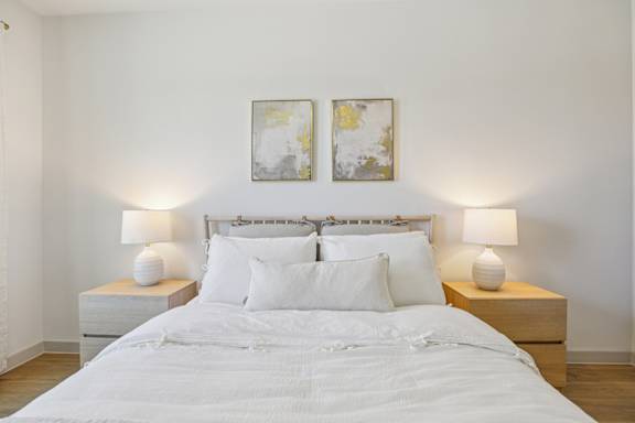 A bed with white bedding and two white lamps on either side. at ThreeTwenty at the Vybe Apartments, Kyle, Texas