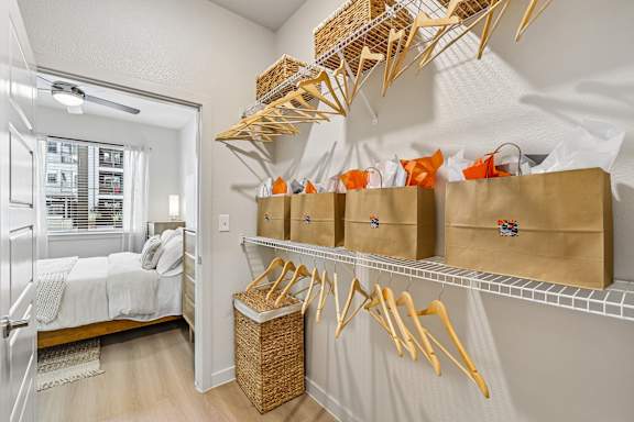 A room with a bed, a window, and a wall-mounted shelf with baskets and bags.
