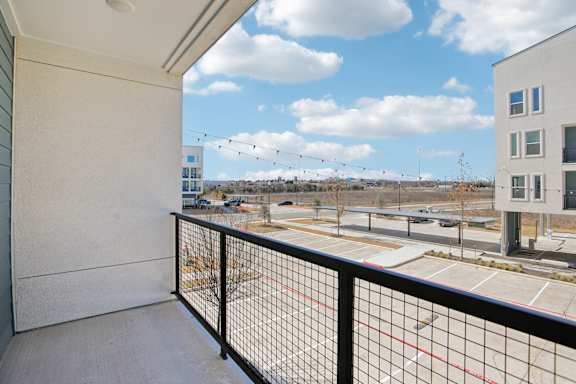 A balcony with a black railing overlooks a parking lot and buildings at ThreeTwenty at the Vybe Apartments, Texas, 78640