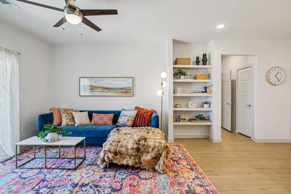 A living room with a blue couch and a colorful rug at ThreeTwenty at the Vybe Apartments, Kyle, TX, 78640