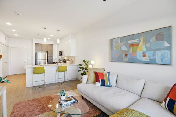 A modern living room with a white couch and a painting on the wall. at ThreeTwenty at the Vybe Apartments, Kyle, TX, 78640