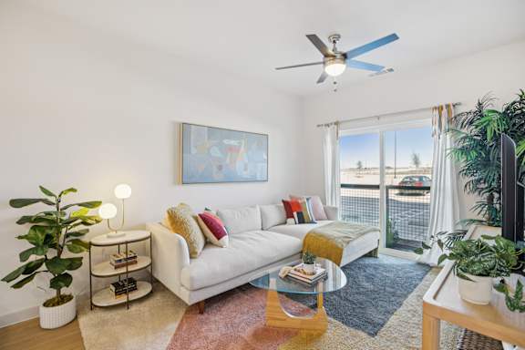A living room with a white couch, a ceiling fan, and a painting on the wall at ThreeTwenty at the Vybe Apartments, Texas