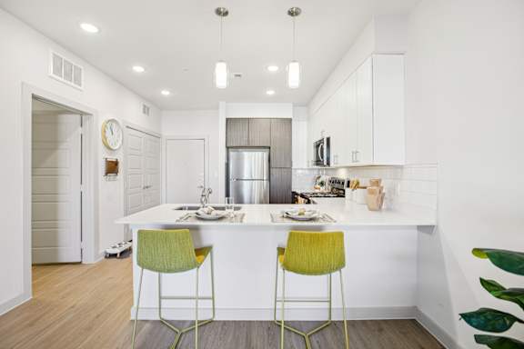 A kitchen with a white counter and two green chairs at ThreeTwenty at the Vybe Apartments, Kyle, TX