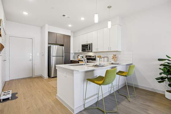 A kitchen with a white island and yellow chairs at ThreeTwenty at the Vybe Apartments, Kyle, 78640