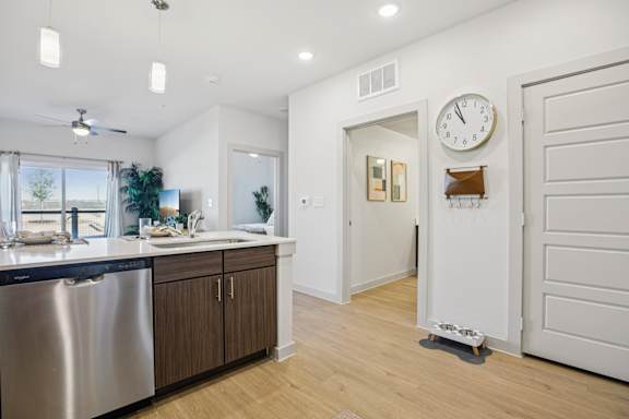 A modern kitchen with a stainless steel dishwasher and wooden cabinets. at ThreeTwenty at the Vybe Apartments, Kyle, TX