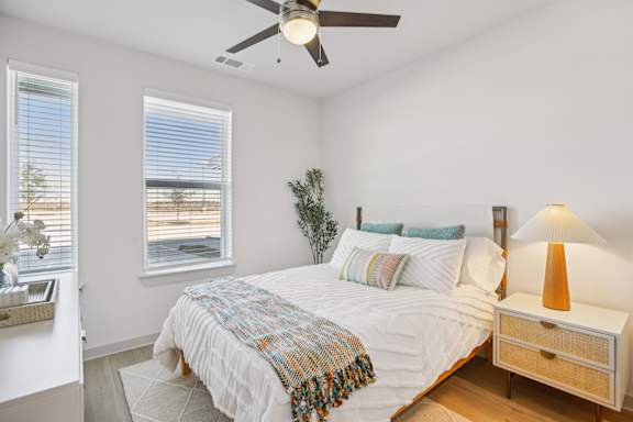 A bedroom with a bed, a ceiling fan, and a nightstand with a lamp. at ThreeTwenty at the Vybe Apartments, Kyle, Texas