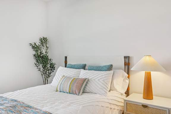 A bed with a white comforter and a white pillow with a blue pillow case on it. at ThreeTwenty at the Vybe Apartments, Kyle
