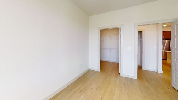 A room with white walls and wooden flooring, with a doorway leading to another room.