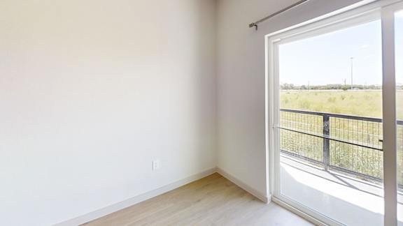 A room with a sliding glass door leading to a balcony with a view of the outdoors.