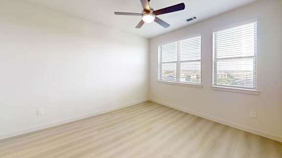 A room with a ceiling fan and two windows.