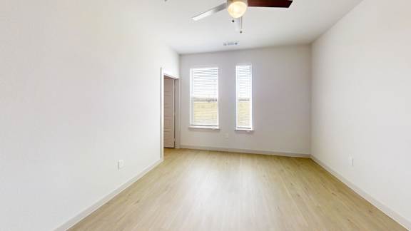 A room with a ceiling fan and two windows.