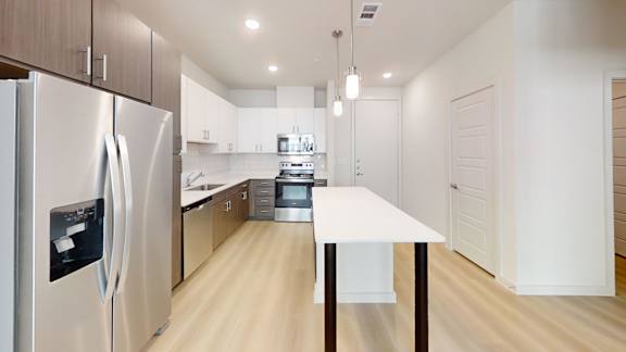 A modern kitchen with a refrigerator on the left and a table in the middle.