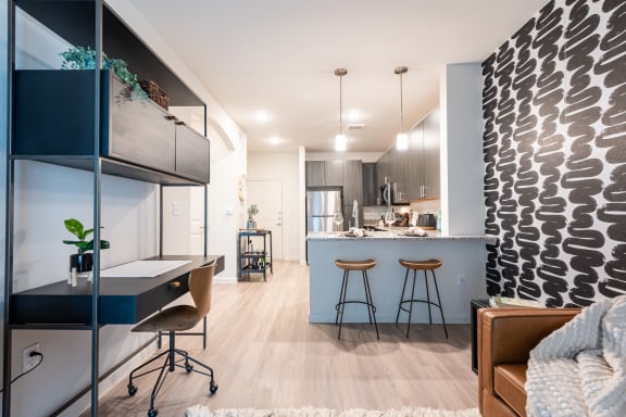 a home office with a desk and stools next to a kitchen with a breakfast bar