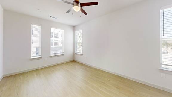 A room with a ceiling fan and three windows.
