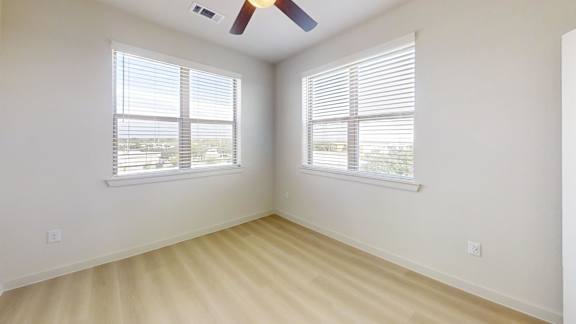 A room with a ceiling fan and two windows with blinds.