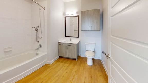 A white toilet sits in a bathroom with wooden floors and white walls.
