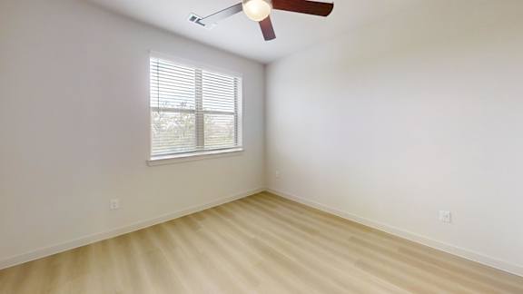 A room with a ceiling fan and a window with blinds.