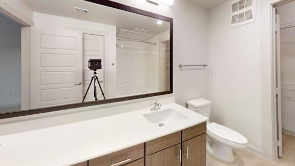 A bathroom with a sink, toilet, and a mirror. at Bridge at Saffron Apartments, Texas