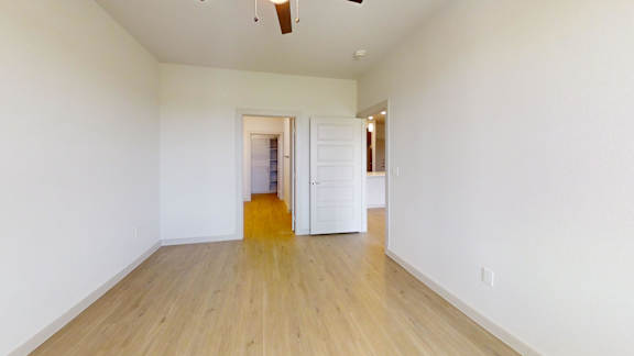 A room with white walls and wooden flooring with a doorway leading to another room.