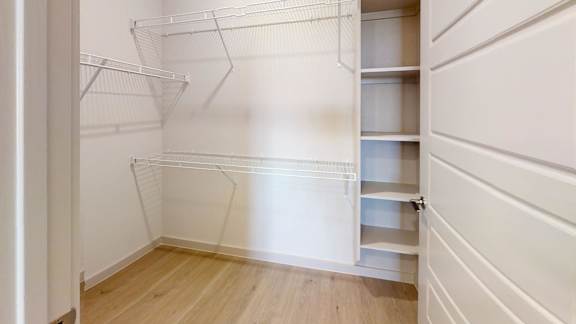 A white walk-in closet with wooden floors and shelves.