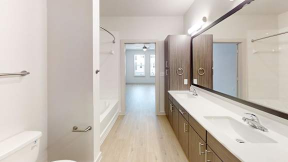 A bathroom with a white tub and sink, wooden floors, and a large mirror.