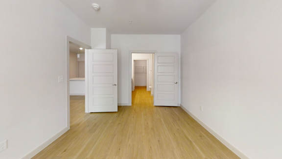 A room with white walls and wooden flooring with a white door on the left and a white wardrobe on the right.