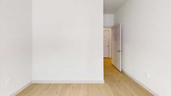 A room with white walls and wooden flooring with a doorway leading to another room.