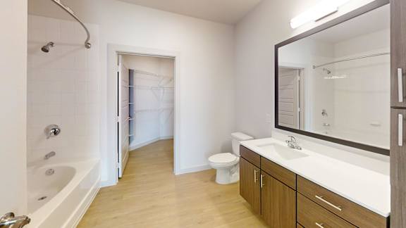 A white bathroom with wooden floors and a white tub.