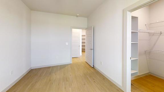 A room with white walls and wooden flooring with a doorway leading to another room.