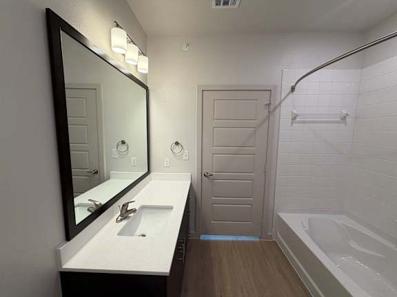 A white bathroom with a sink, mirror, and bathtub.